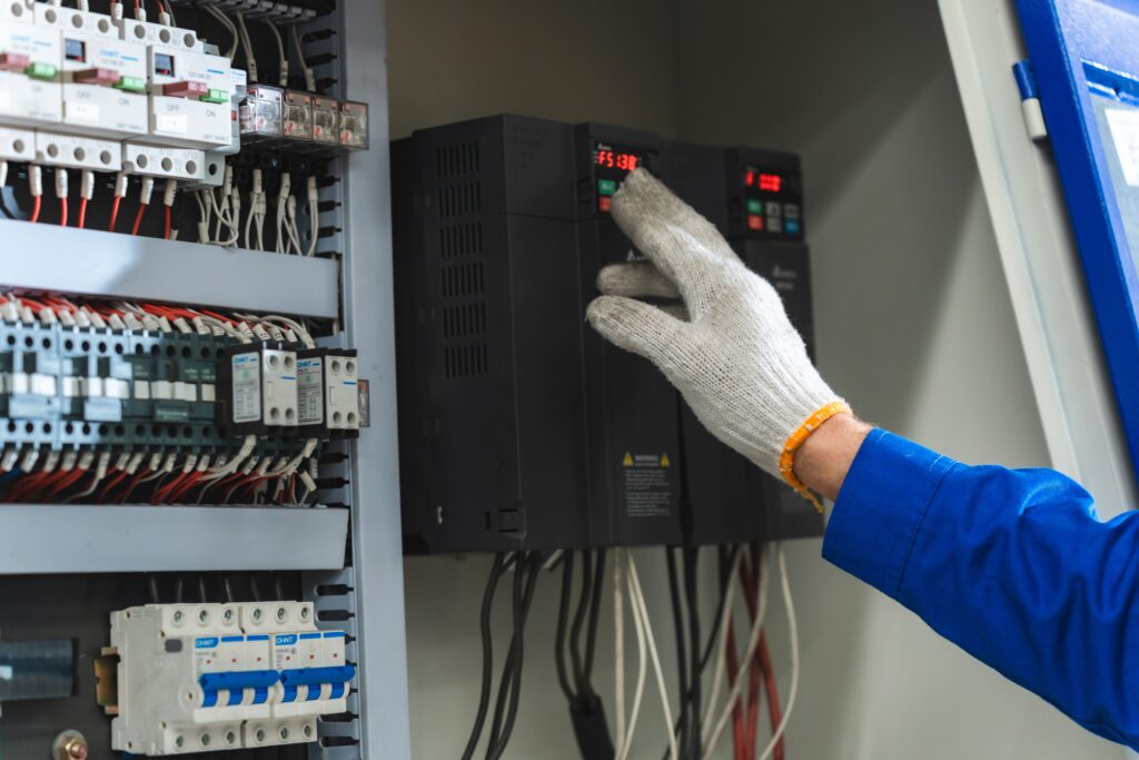 Técnico ajustando un variador de frecuencia en cuadro eléctrico industrial — ingeniería electromecánica