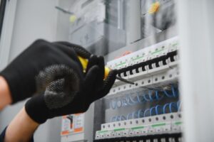 Técnico eléctrico ajustando interruptores automáticos en cuadro de distribución de baja tensión con cableado azul — mantenimiento eléctrico BT industrial VOLTIA