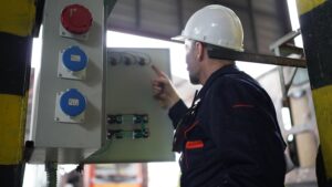 Técnico eléctrico con casco inspeccionando cuadro de control y tomas industriales en planta de producción — mantenimiento de protecciones eléctricas industriales VOLTIA